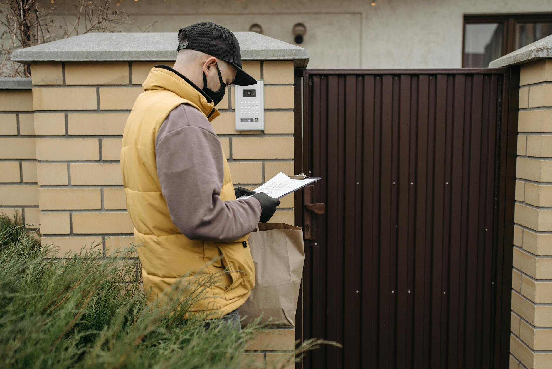 Kurier w maseczce dostarcza paczkę pod bramę prywatnego domu