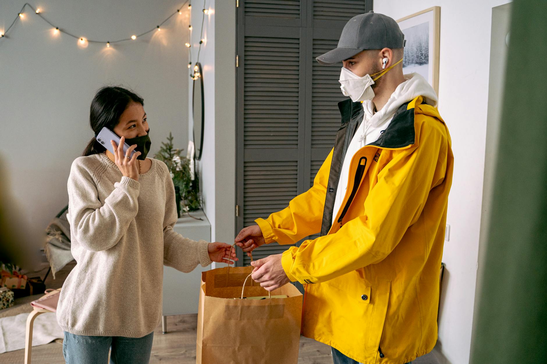 Kobieta odbiera bezdotykową przesyłkę od kuriera przed domem